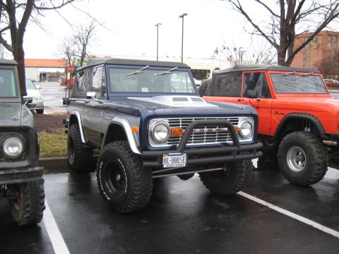 1994 Ford Bronco - Two Ford Broncos, one blue and one orange, are parked side-by-side in a lot.