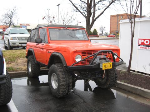 1994 Ford Bronco - This orange Ford Bronco features a winch and large off-road tires, parked next to another vehicle.