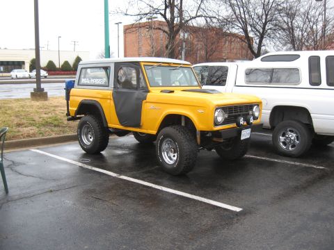 1994 Ford Bronco - Yellow Ford Bronco with aftermarket soft doors and lifted suspension parked in a lot.