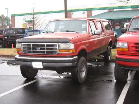 1994 Ford Bronco - A red Ford Bronco is parked in a lot next to another vehicle.