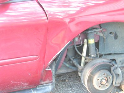 1997 Ford Taurus - Close-up of a damaged red car fender and exposed wheel assembly.