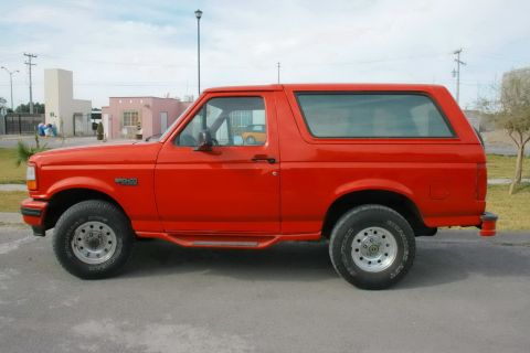 1995 Ford Bronco - A red Ford Bronco SUV is parked on a street, viewed from the side.