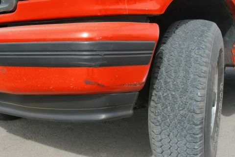 1995 Ford Bronco - The front corner of an orange SUV shows some wear and tear on the fender and bumper trim.