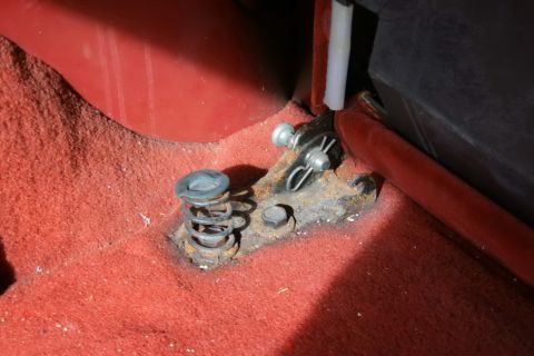 1995 Ford Bronco - Close-up view of a rusted seat mounting bracket with a spring mechanism on red carpet inside a vehicle.