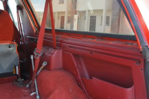 1995 Ford Bronco - Interior view of a red SUV, showing the seatbelt and tools on the floor, with houses visible through the window.