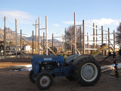 1995 Ford Bronco - A blue Ford tractor sits in a dirt lot with mountains in the background and a partially constructed wooden frame.