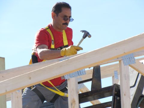 1995 Ford Bronco - A worker hammers wooden beams while wearing a safety harness against a clear blue sky.