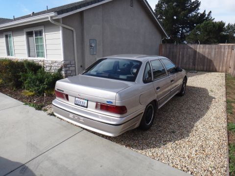 1993 Ford Taurus - Rear view of a 1993 Ford Taurus sedan parked in a gravel driveway next to a house.