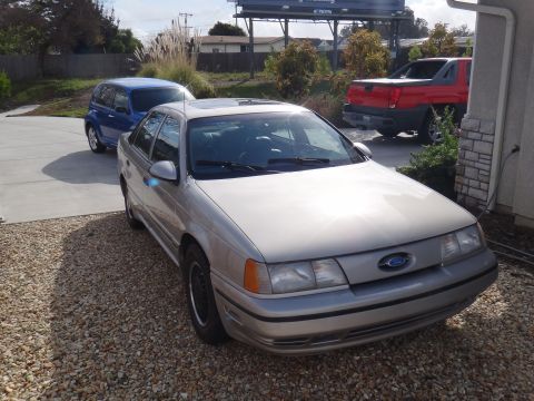 1993 Ford Taurus - A silver sedan is parked in a driveway next to a blue hatchback and a red pickup truck.