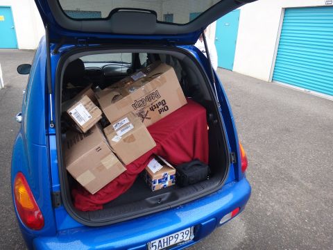 1993 Ford Taurus - Blue Chrysler PT Cruiser loaded with boxes in its trunk, parked outdoors near storage units.
