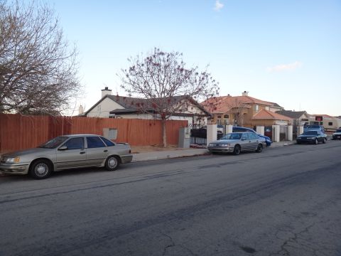 1993 Ford Taurus - A gold sedan is parked on the street in front of a wooden fence and houses.