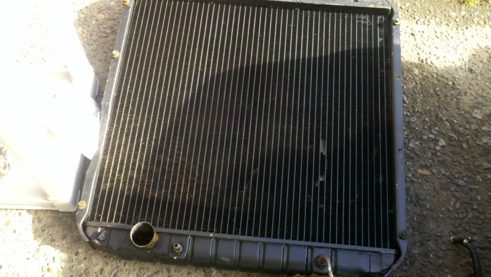 Radiator with black fins and metal tanks, lying on gravel
