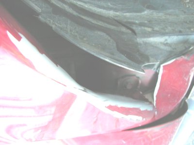 1997 Ford Taurus - Close-up view of a damaged red car fender, revealing exposed mechanical parts and chipped paintwork.