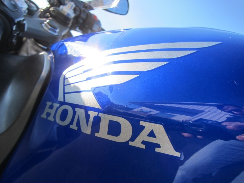 Blue Honda motorcycle fuel tank with silver wing logo and "HONDA" text. Part of handlebars visible