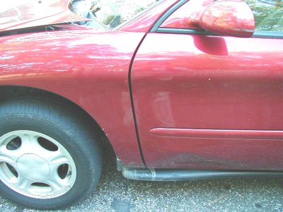 1997 Ford Taurus - The side profile of a red 1997 Ford Taurus is visible, focusing on the front fender and driver's side door.