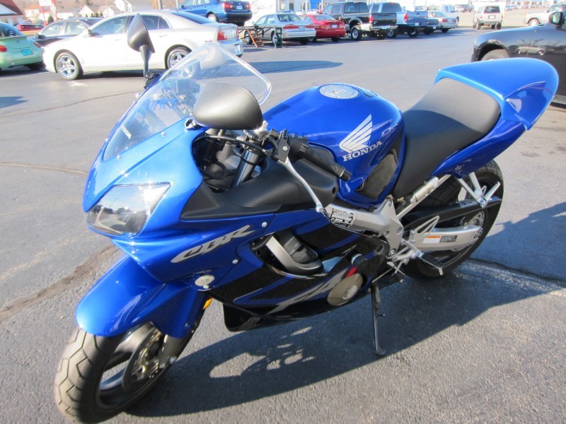 Blue Honda CBR motorcycle parked on asphalt, with other cars in the background