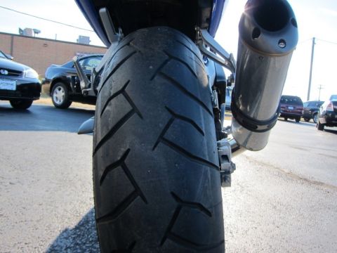1999 Mercury Grand Marquis - Close-up of a motorcycle's rear tire and exhaust system, with other vehicles visible.