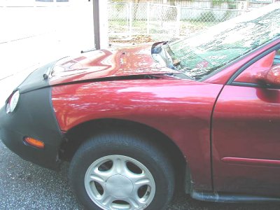 1997 Ford Taurus - The front end of a red sedan is covered by a car bra, with visible damage to the hood.