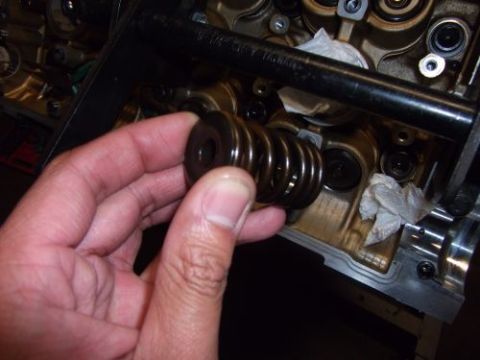 1991 Ford Taurus - A hand holds an engine valve spring, with the engine block and camshaft visible in the background.