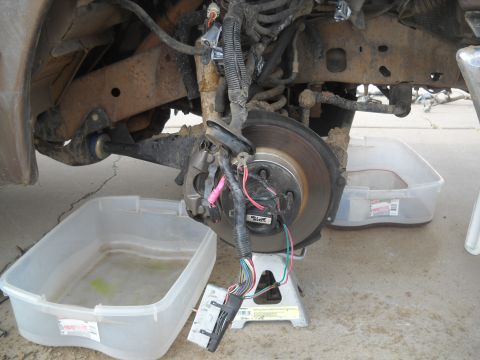 1992 Ford Explorer - Front wheel assembly with brake rotor and wiring harness, supported by a jack stand, with collection bins underneath.