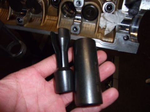 1991 Ford Taurus - Engine valve spring compressor tool and socket held near an engine block.