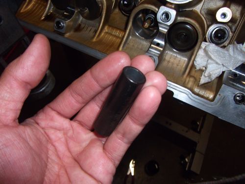 Hand holding valve tappet, engine block visible
