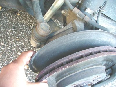 1997 Ford Taurus - A hand inspects a worn brake rotor and associated suspension parts, suggesting a potential mechanical issue.
