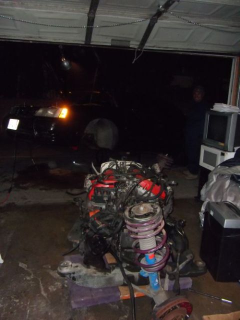 1991 Ford Taurus - An engine and suspension assembly sits on the floor of a garage, with a car in the background.