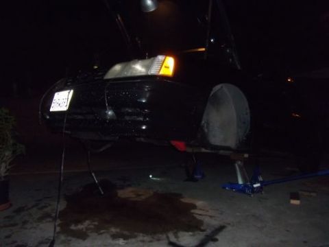1991 Ford Taurus - A black car is elevated on jack stands, with its front end disassembled for maintenance.