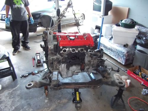Engine assembly with red valve covers suspended by chains, resting on a metal frame with jacks