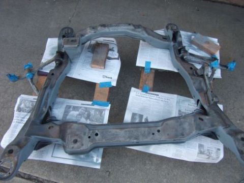 1991 Ford Taurus - A vehicle subframe is shown on newspapers, secured with blue tape and wooden blocks.