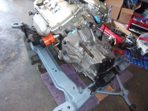 1991 Ford Taurus - Engine and subframe assembly, likely for a vehicle, is shown in a garage setting.