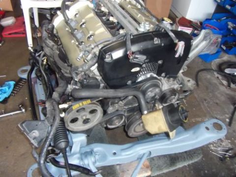 1991 Ford Taurus - Engine assembly with black covers and silver valve covers, mounted on a gray frame.