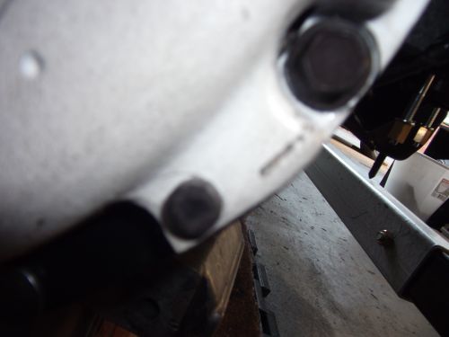 Close-up of a white engine component with bolts, on a metal stand
