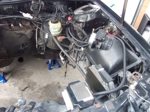 Engine bay with brake master cylinder, air intake, and wiring visible. Car is on jack stands