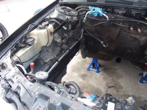 Car engine bay with parts removed, supported by jack stands