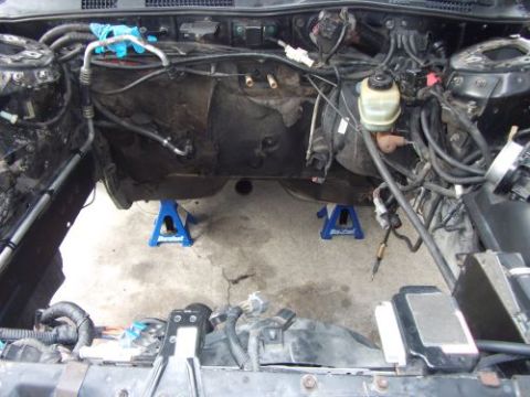 1991 Ford Taurus - The engine bay of a vehicle is shown with the engine removed, supported by blue jack stands.