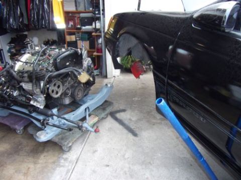 1991 Ford Taurus - Engine removed from a black car, with the engine assembly resting on a dolly nearby.