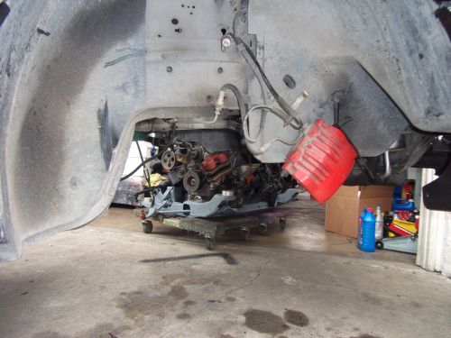 engine on a dolly under a car's wheel well, red brake caliper hanging nearby