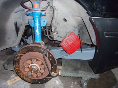 1991 Ford Taurus - A close-up view of the front suspension and brake assembly of a vehicle, featuring a blue Tokico shock absorber, a rusted brake rotor with…