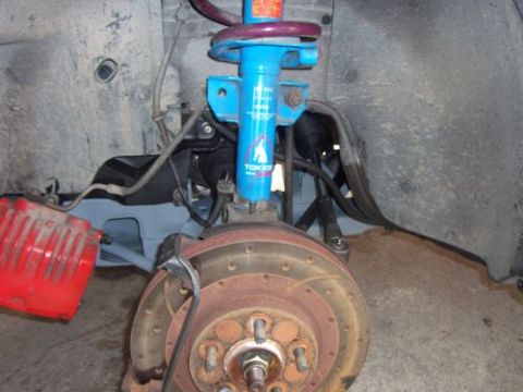 1991 Ford Taurus - Close-up view of a vehicle's front suspension system, a blue shock absorber and a red brake caliper.