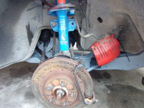 1991 Ford Taurus - A close-up view of the front suspension and braking system of a vehicle, featuring a blue shock absorber, a red brake caliper, and a rusty…