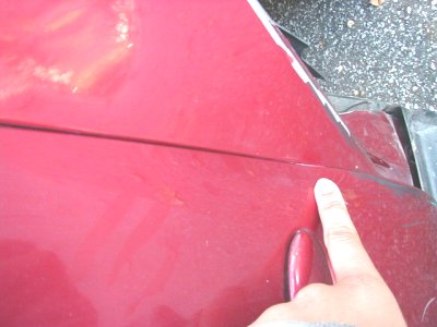 1997 Ford Taurus - A finger points to a noticeable gap between the red body panels of a car.