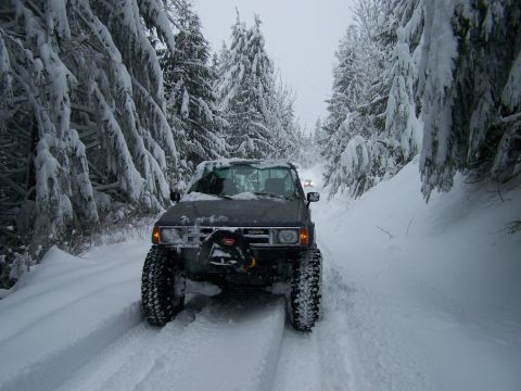 1988 Suzuki Samurai - A lifted pickup truck navigates a snow-covered forest road, with another vehicle visible ahead.