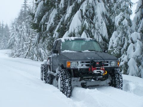 1988 Suzuki Samurai - A Toyota pickup truck navigates a snowy forest road with its front winch engaged.