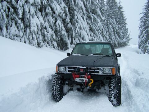 1988 Suzuki Samurai - This Toyota pickup truck navigates a snow-covered road surrounded by snow-laden trees.