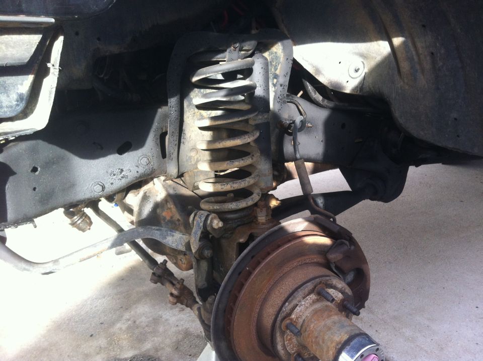 Close-up of front suspension, coil spring, brake rotor, and steering linkage on a vehicle