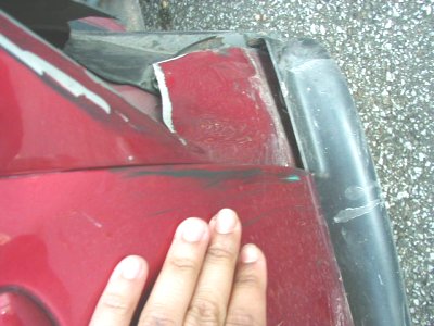 1997 Ford Taurus - Damage to the fender of a red car is visible, with a hand resting on the surface.