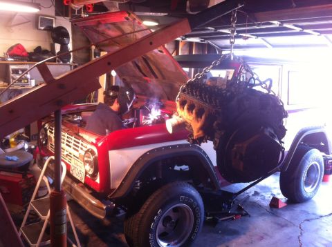 1968 Ford Bronco - A 1968 Ford Bronco is undergoing engine work in a garage, with a welder and engine hoist present.