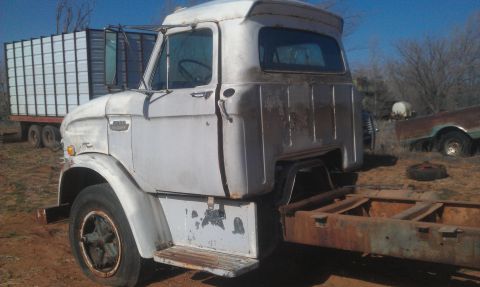 1973 Ford F-100 - A white 1961 Ford F-series truck cab sits in a field next to a trailer, with another vehicle visible in the background.